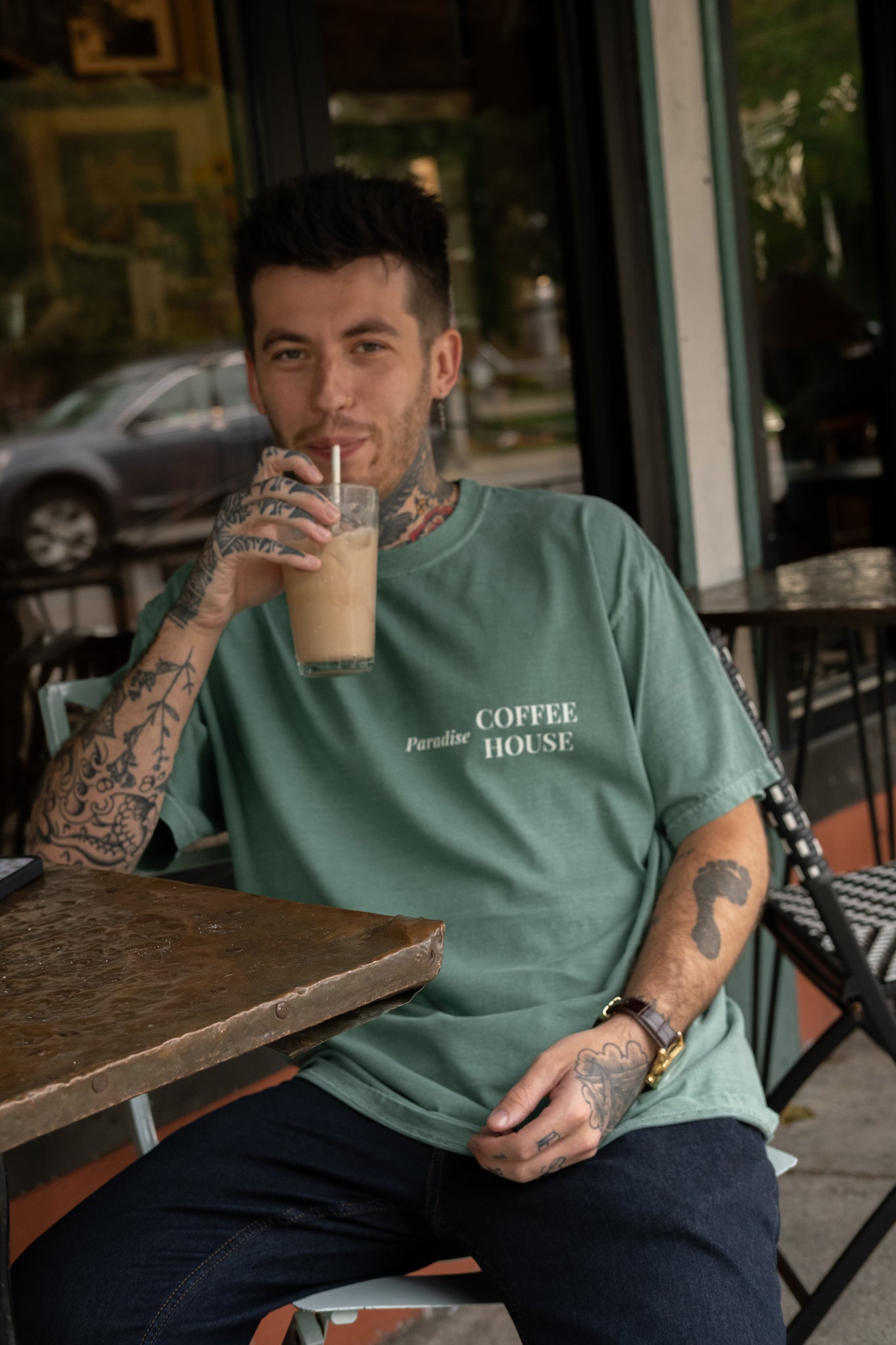 tatted guy drinking coffee wearing paradise coffee house oversized aesthetic shirt from small business raye of happiness