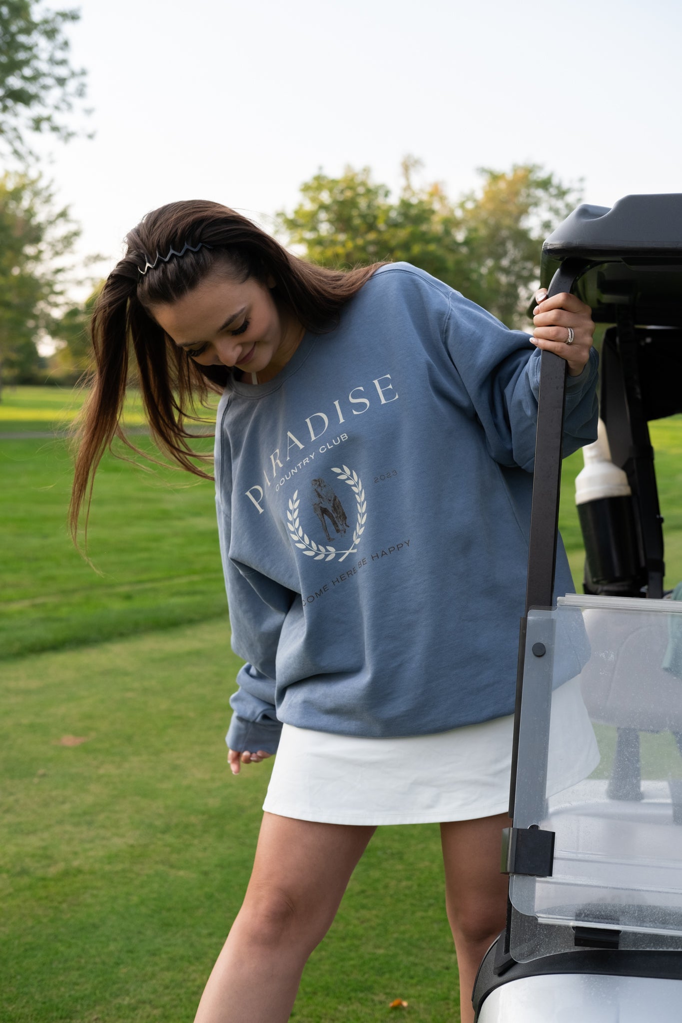 cute girl wearing a paradise country club aesthetic crewneck on a golf course
