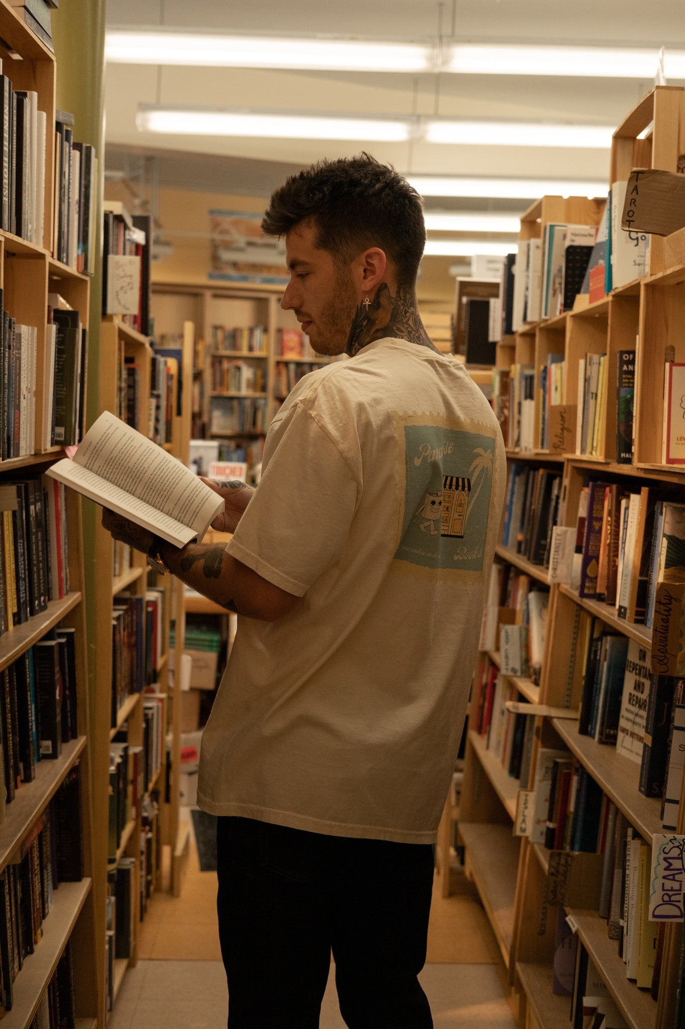 tatted boy wearing a paradise book store aesthetic oversized tee from small business raye of happiness